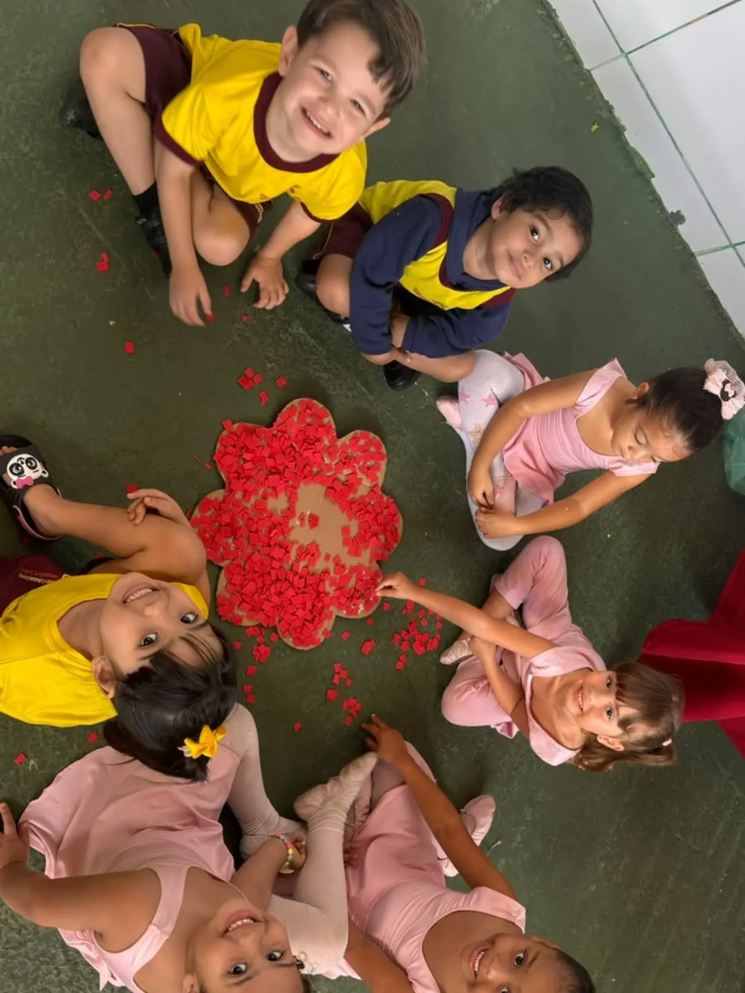 Vista de cima de uma roda de crianças em volta de uma flor grande feita de papel vermelho picado