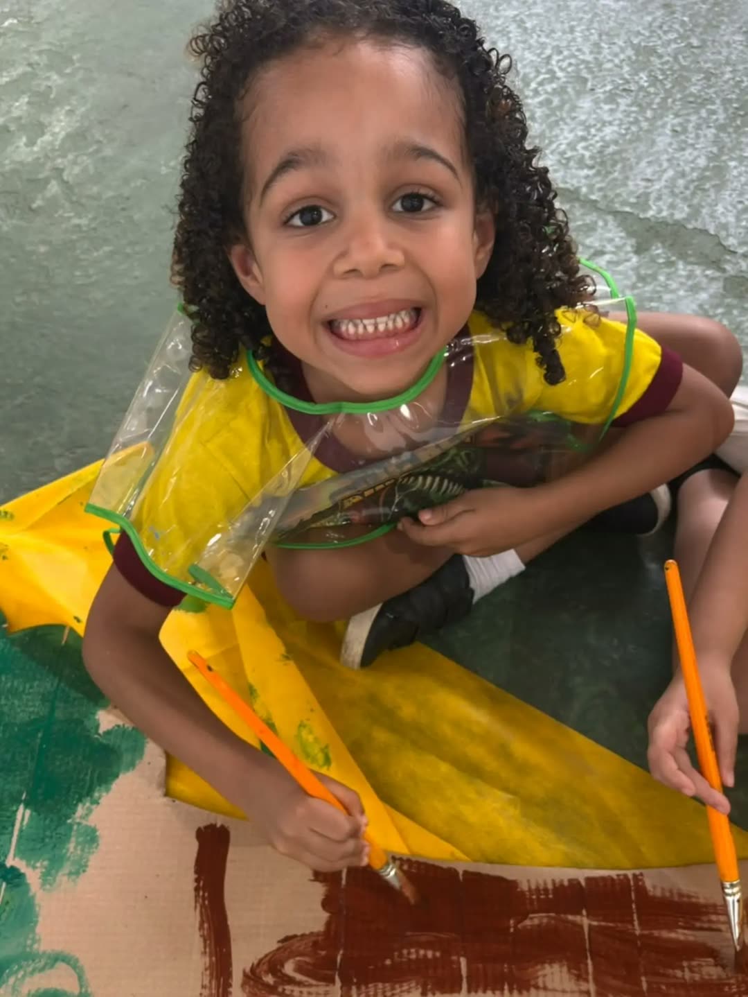 Menina de cabelo cacheado sorrindo de orelha a orelha com o pincel na mão